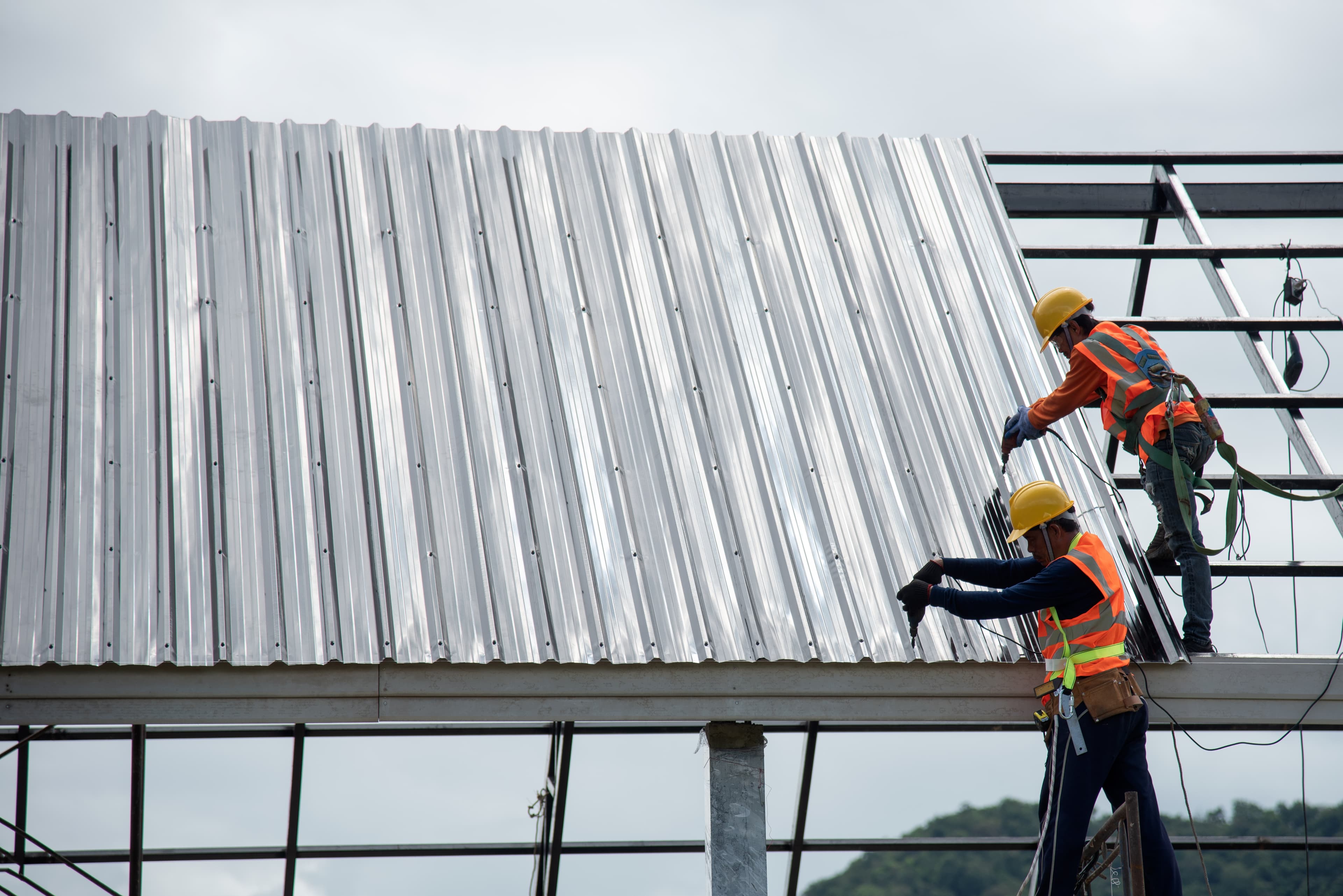Two roofers installing standing-seam metal panels on a commercial building
